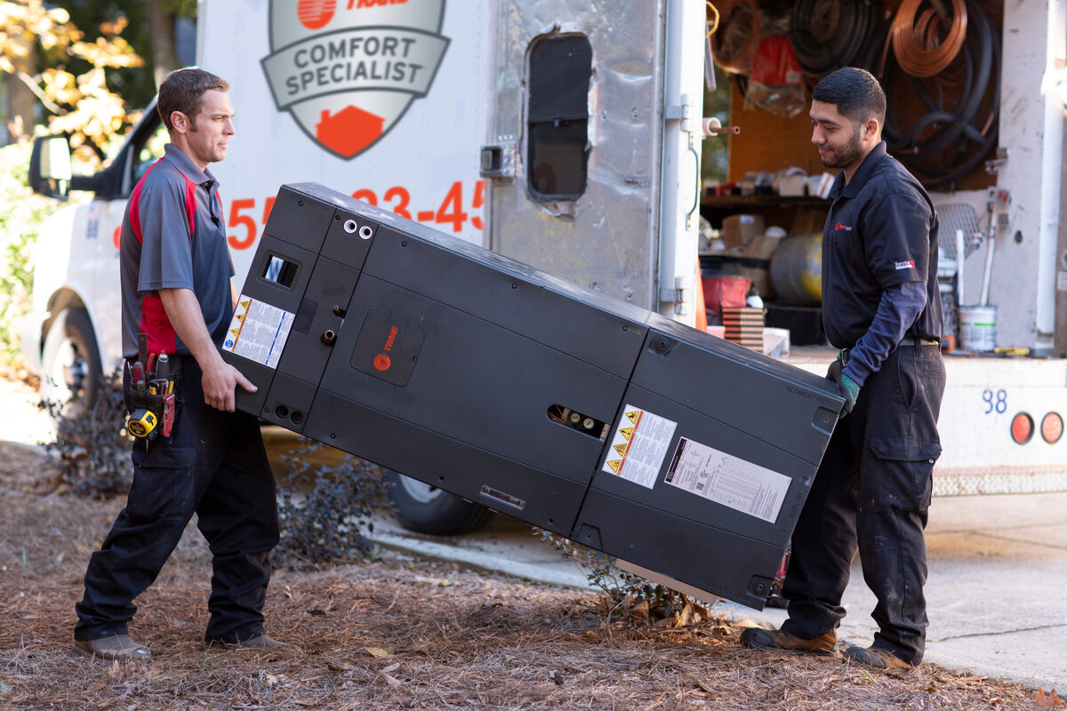 technicians walking a heat pump out of a truck into a house